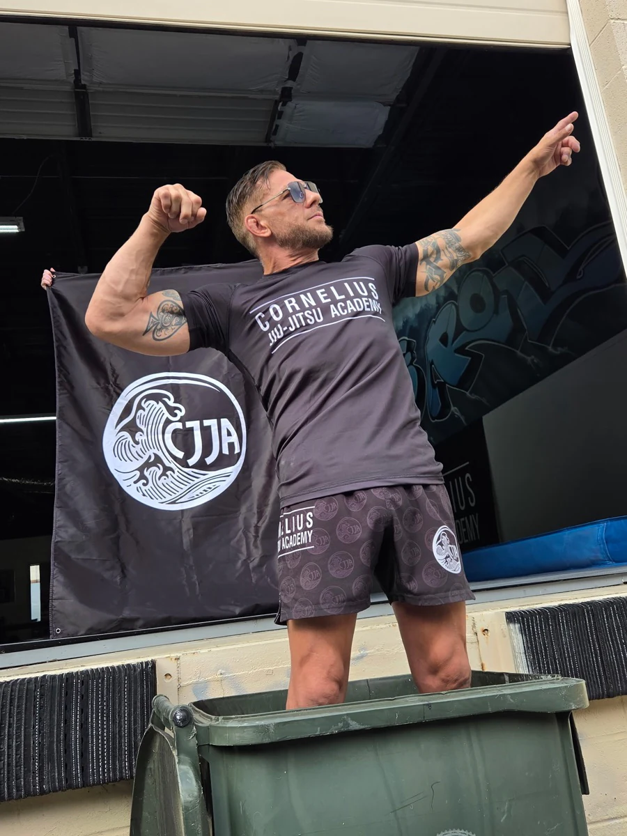 A teammate in CJJA gear posing in front of the academy flag