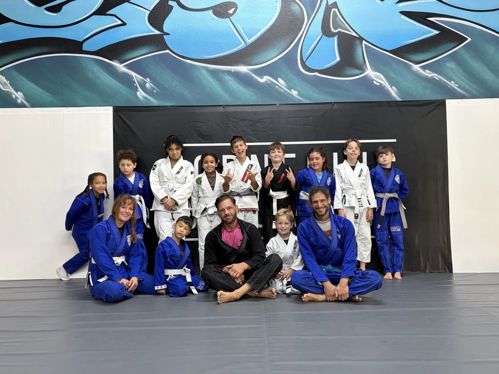 Kids and coaches posing together in gis in front of the academy banner