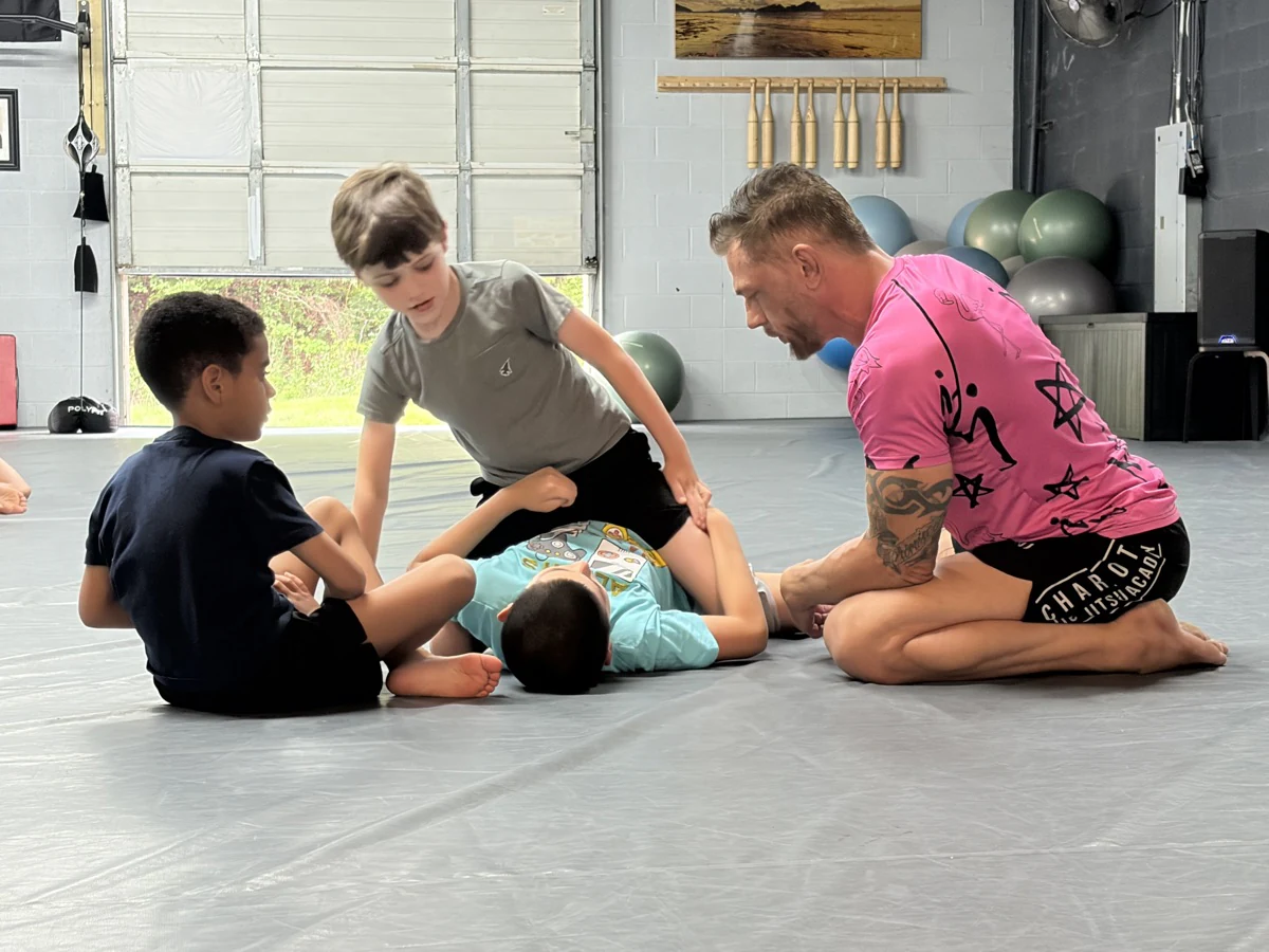 A coach guiding three children through a ground position