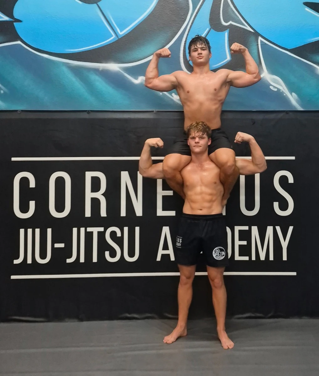 Two teammates flexing with one seated on the other’s shoulders at CJJA