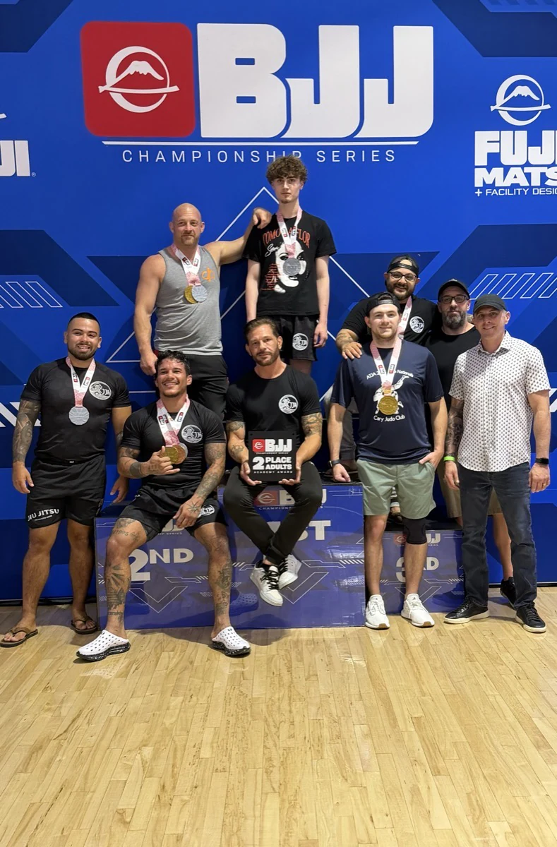 A group posing with medals and a team award at a jiu-jitsu tournament